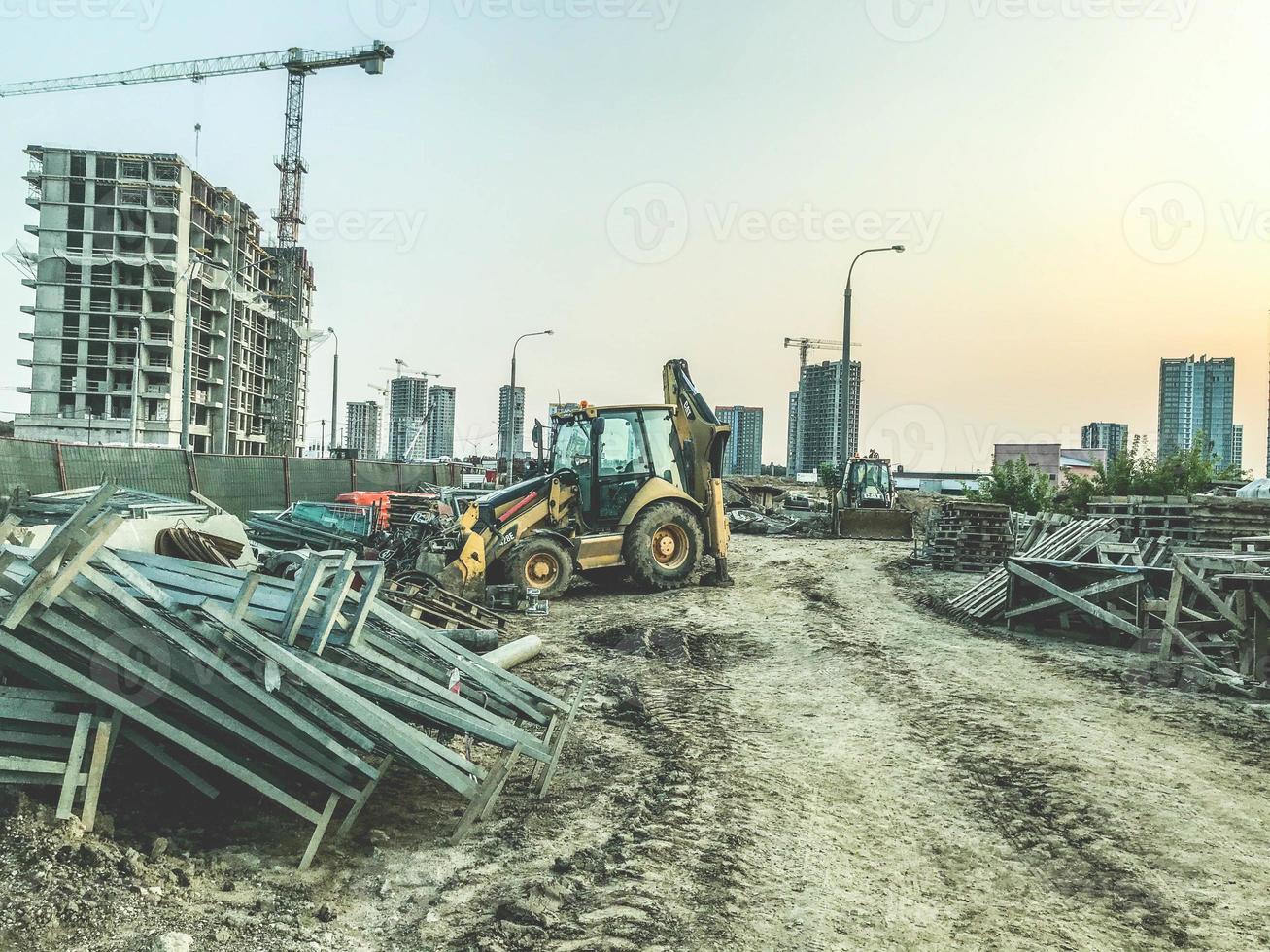 bouw plaats van een nieuw wijk. geel bouw uitrusting en gebouw materialen Aan plaats. tegen de achtergrond van hoog huizen. bouw kranen zijn gebouw een buurt foto