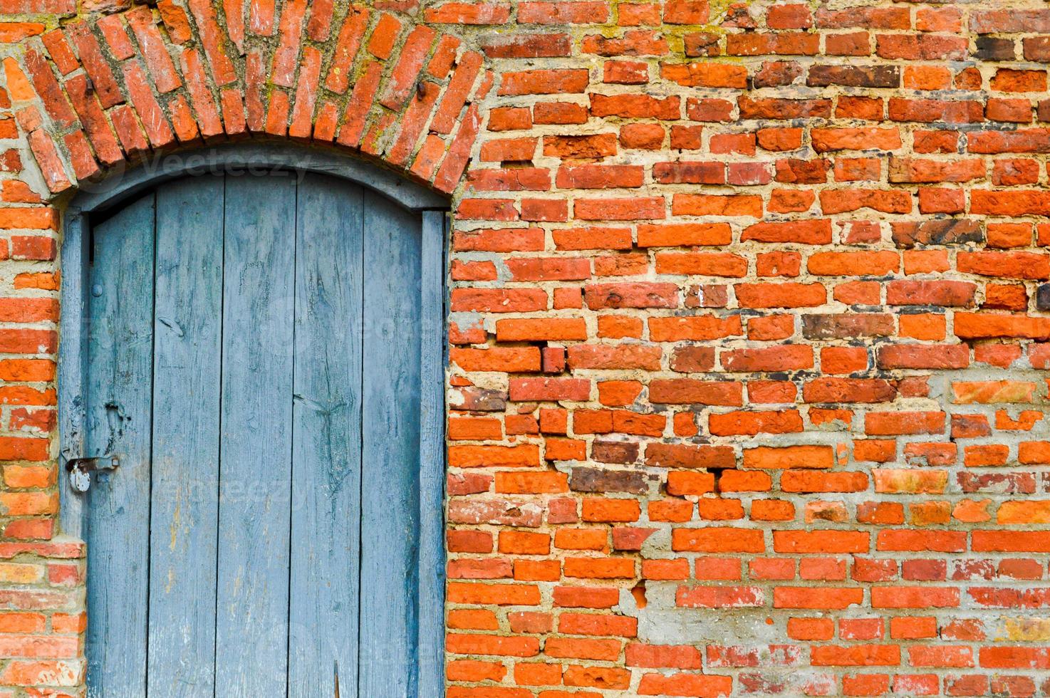 de structuur van de oud oude middeleeuws antiek solide houten natuurlijk dik deur met klinknagels en nagels patronen en sloten gemaakt van houten planken tegen de achtergrond van een steen muur van rood steen foto