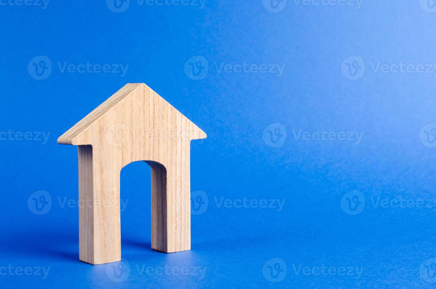 houten figuur van een huis met een groot deuropening Aan blauw achtergrond. concept van buying en verkoop echt landgoed, huur, investering. huis, betaalbaar huisvesting, woon- gebouw. bouw gebouwen. foto