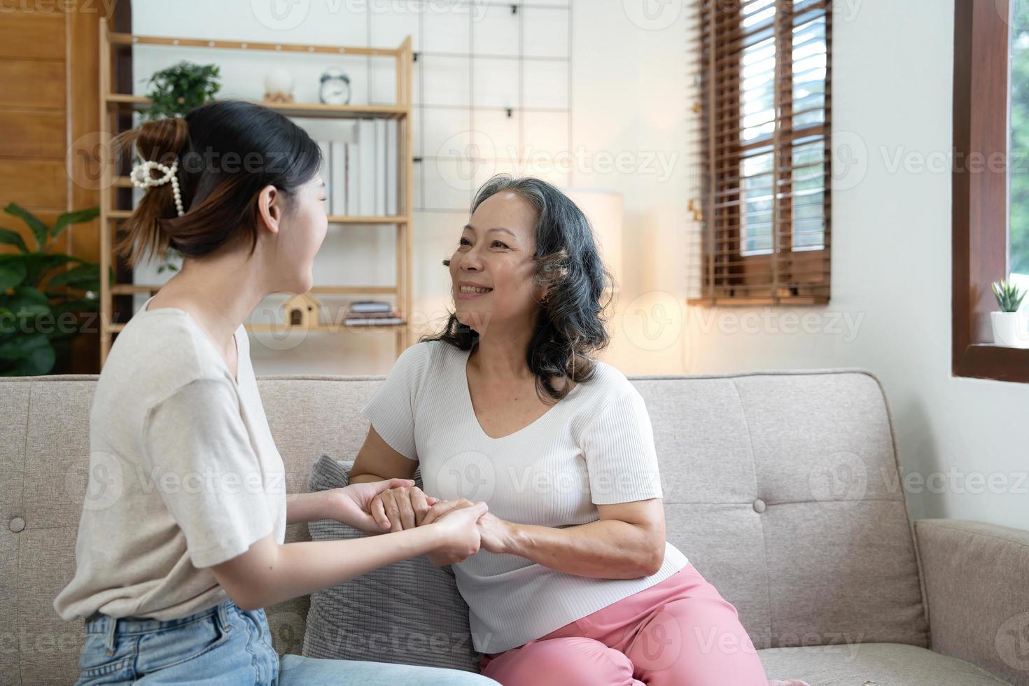 gelukkig volwassen kleindochter en senior grootmoeder hebben pret genieten van praten zitten Aan sofa in modern leven kamer, glimlachen oud moeder knuffelen jong gegroeid dochter bonding chatten ontspannende Bij huis samen foto