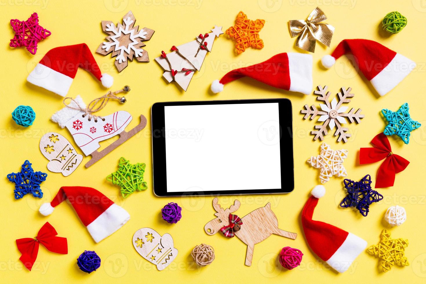 top visie van digitaal tablet met Kerstmis decoraties en de kerstman hoeden Aan geel achtergrond. gelukkig vakantie concept foto