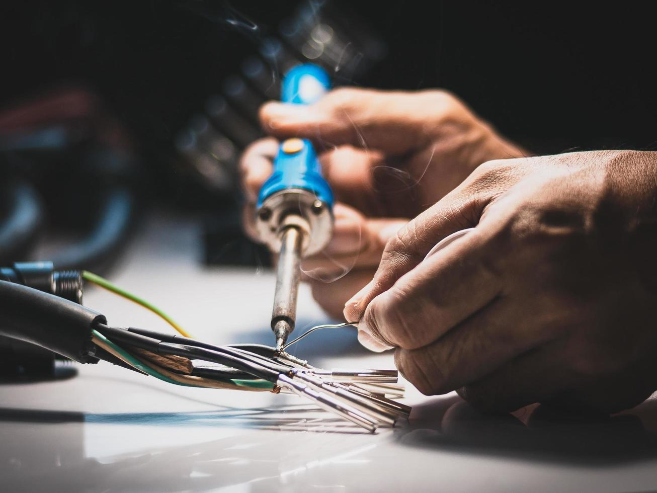 elektricien die een soldeerbout gebruikt om de draden met de metalen pin te verbinden foto