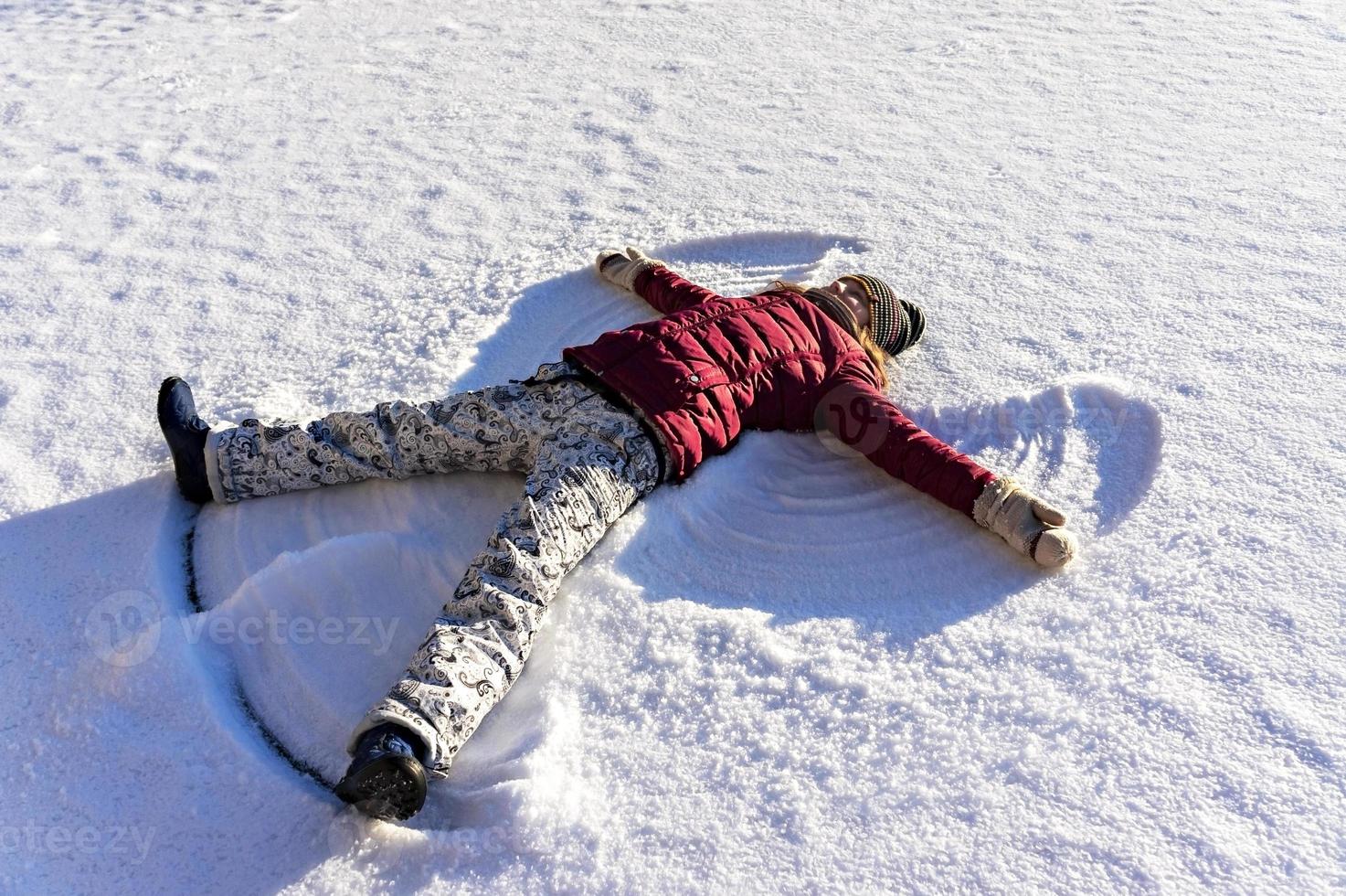 jong vrouw aan het liegen in de sneeuw en maken een sneeuw engel. winter wandelingen en pret foto