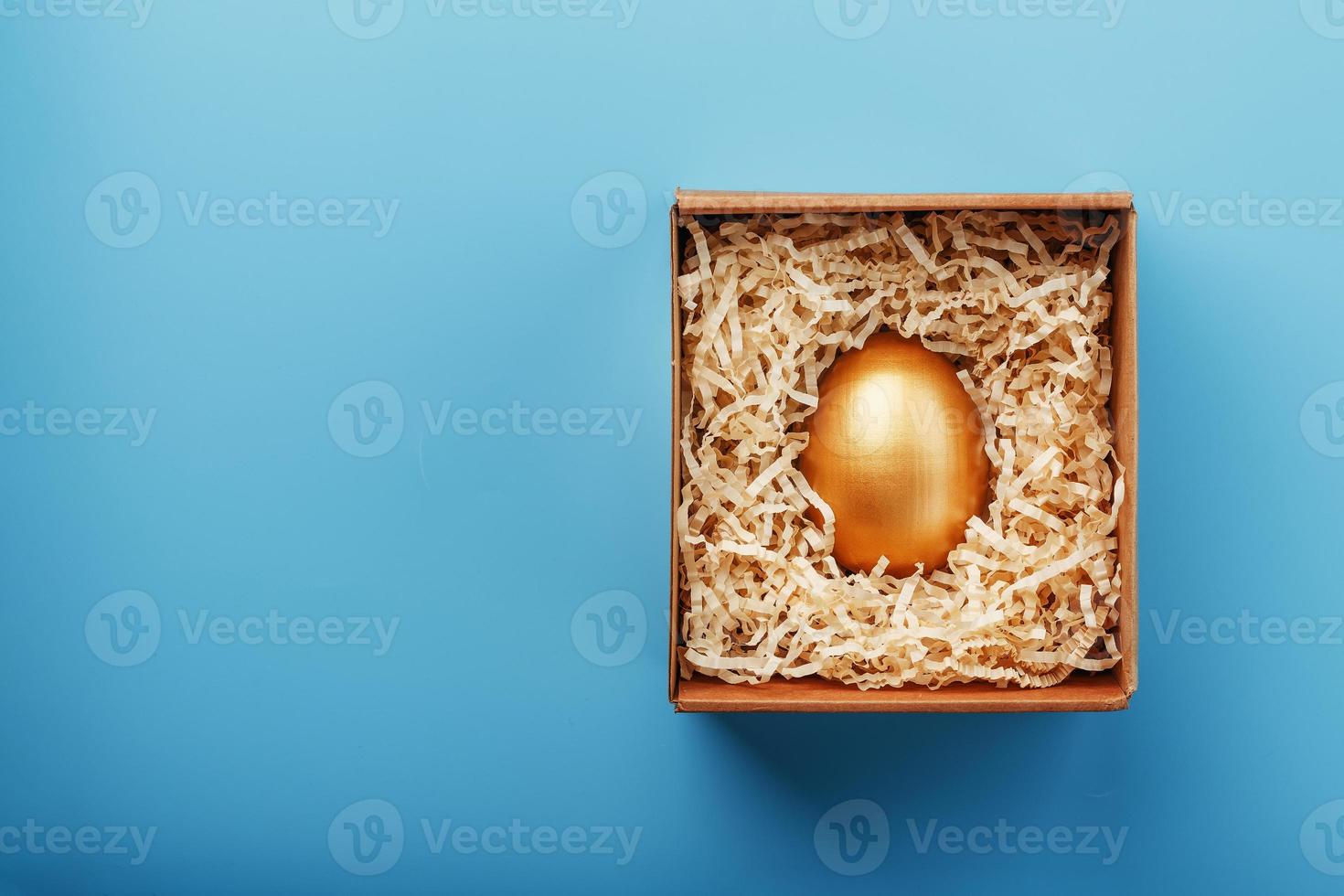 gouden ei in een karton doos met krullen Aan een blauw achtergrond. foto