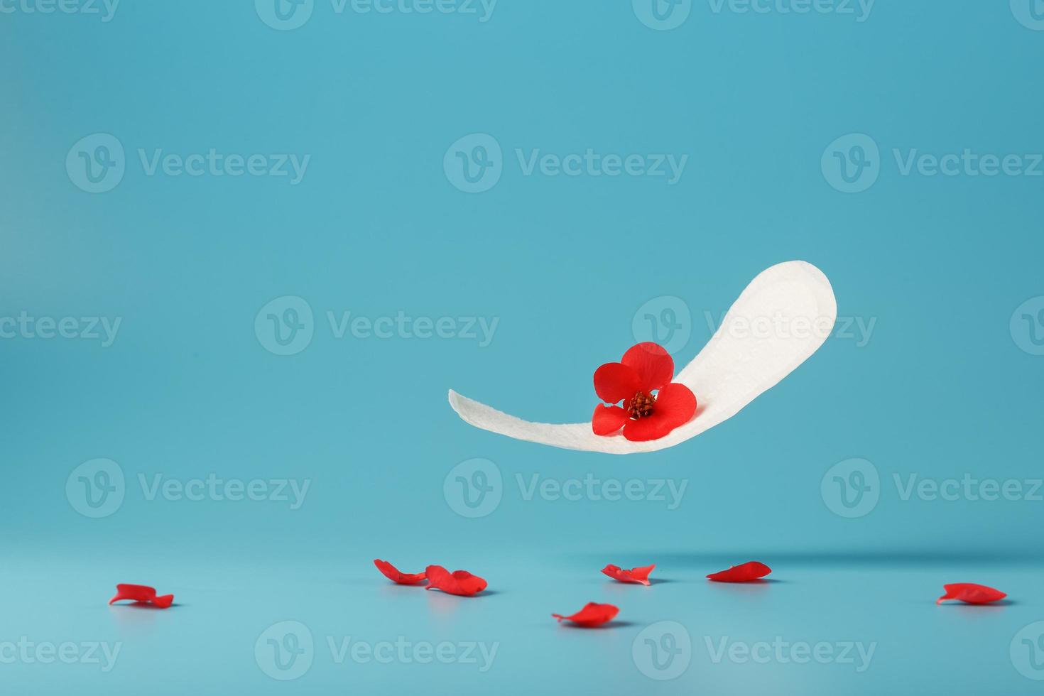 sanitair stootkussen in vlucht Aan een blauw achtergrond met gedaald bloemblaadjes van rood bloemen. concept van de begin van menopauze. foto