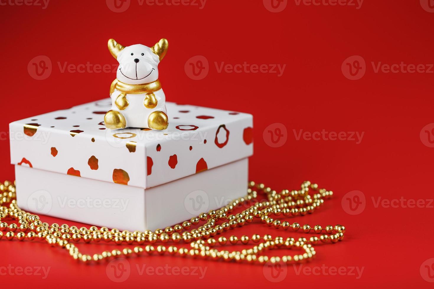 nieuw jaar 2021 speelgoed- stier met een geschenk Aan een rood achtergrond. geschenk doos en goud kralen. foto