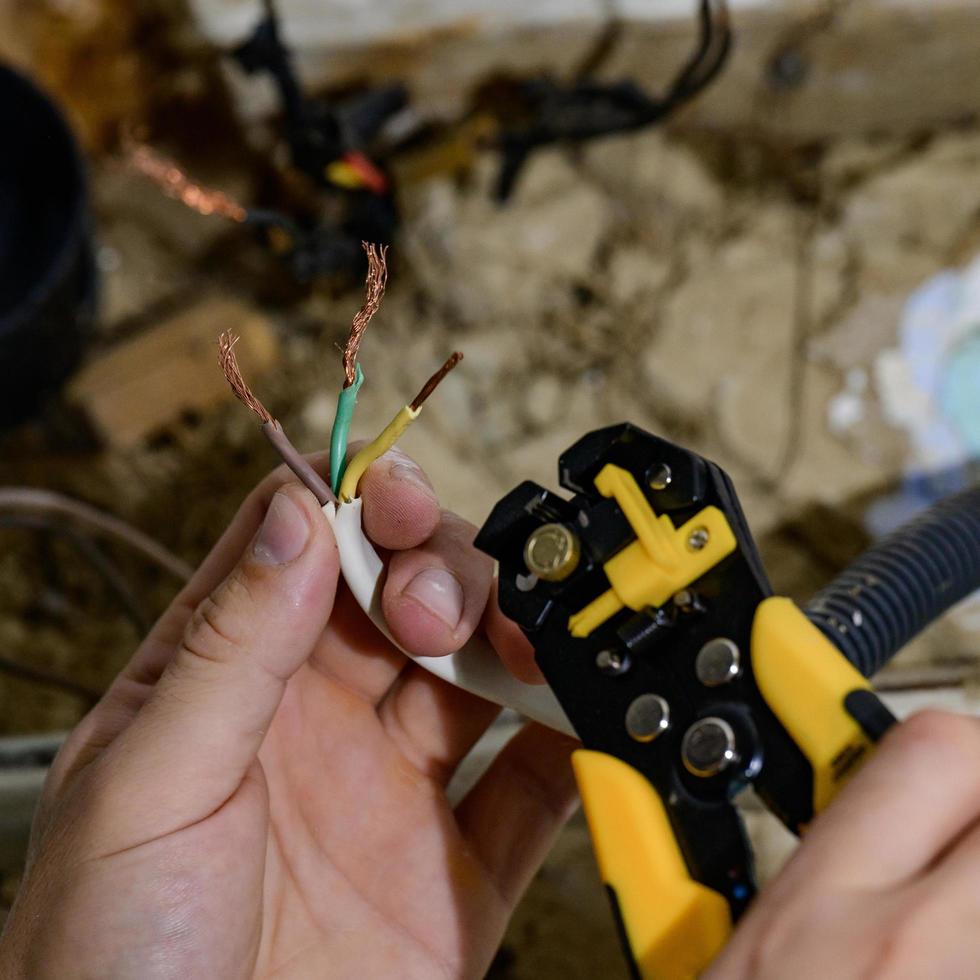 gebruik van de gereedschap voor verwijdering van isolatie voor verwijdering van de einde van een elektrisch draad gedurende reparatie en updaten van elektrisch bedrading in een huis elektrisch netwerk, elektrisch werken. foto