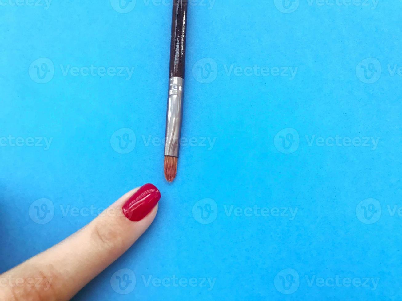 Aan een blauw matte achtergrond maken een helder rood manicuren. nagels zijn geschilderd met een dun borstel met natuurlijk borstelharen. elegant nagel ontwerp, modieus kleuren voor manicure foto