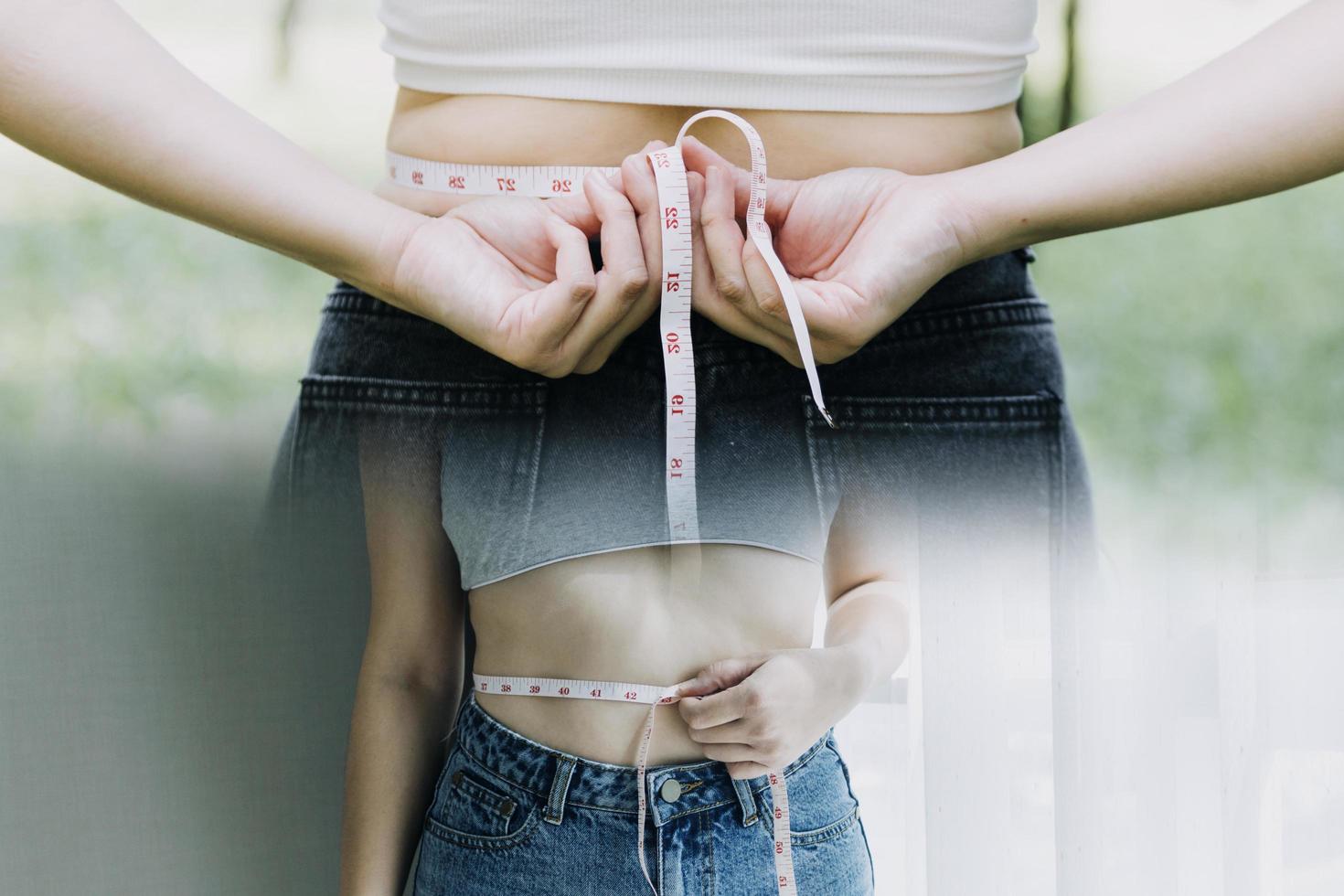 mooie dikke vrouw met meetlint ze gebruikt haar hand om het overtollige vet dat op een witte achtergrond is geïsoleerd uit te knijpen. ze wil afvallen, het concept van chirurgie en vet afbreken onder de foto