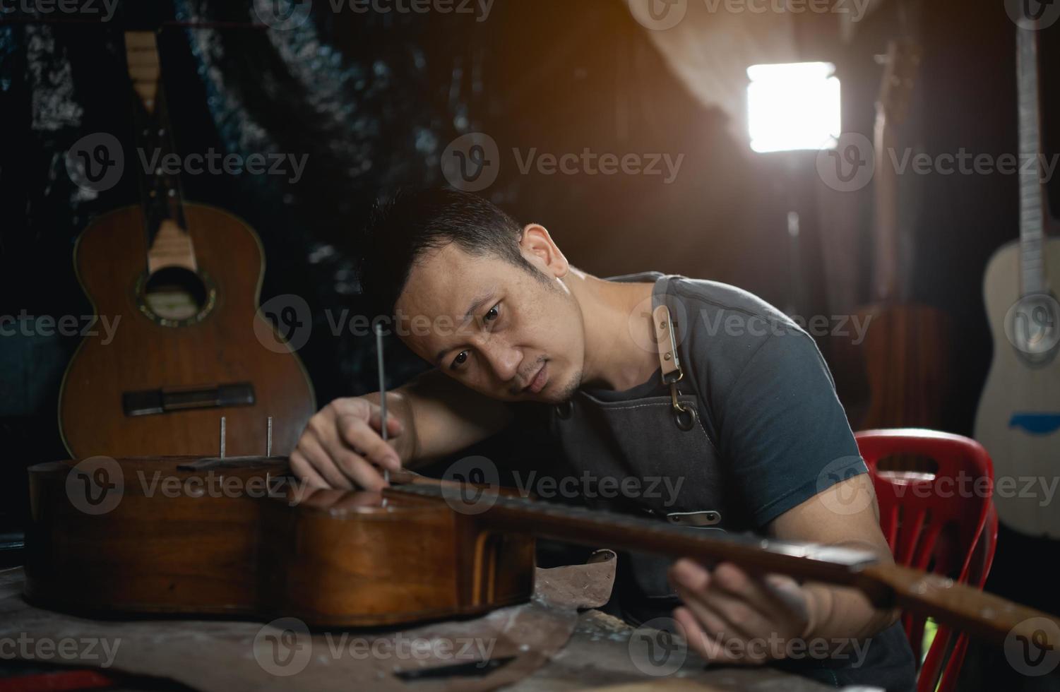 gitaar makers Aziatisch Mens maken akoestisch gitaren in laboratorium. Aziatisch gitaar maker bouwt hoog kwaliteit gitaren voor muzikanten handgemaakt gitaar winkel. werken prima houtmuziek, traditie, oude ambachten. foto