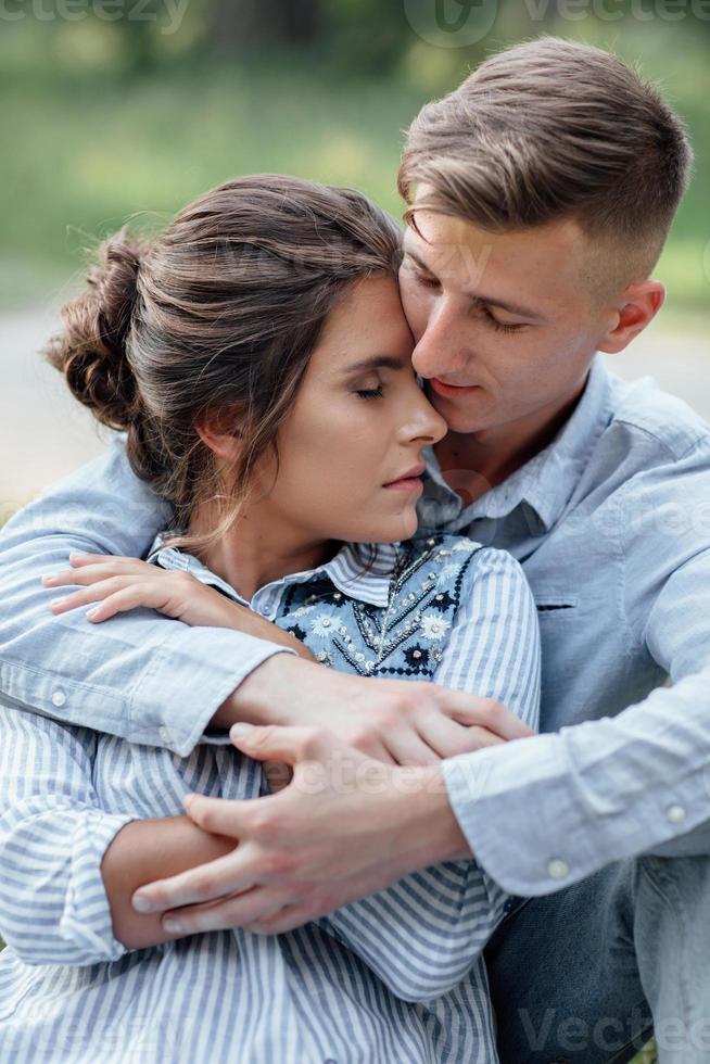 buitenshuis schot van jong gelukkig paar in liefde zittend Aan gras Aan natuur. Mens en vrouw knuffelen, zonlicht in zomer park. gelukkig familie in de avond zon licht. de concept vakantie foto