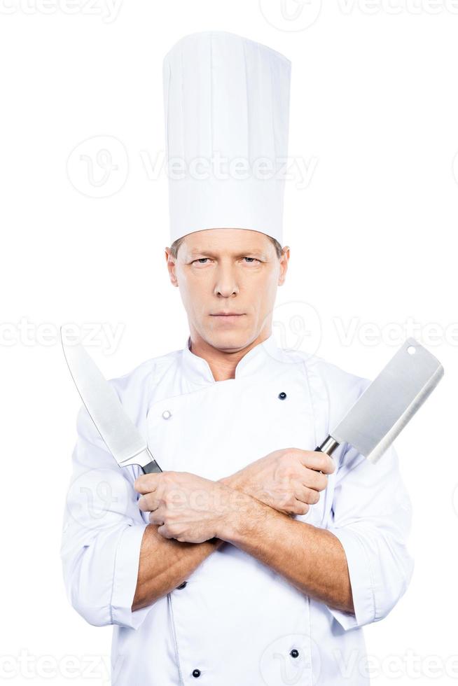 klaar naar werk. zelfverzekerd volwassen chef in wit uniform Holding messen in zijn handen en op zoek Bij camera terwijl staand tegen wit achtergrond foto