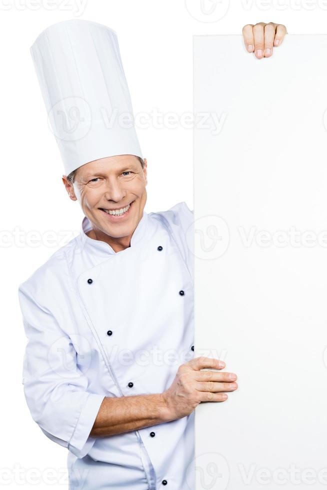 koks keuze. zelfverzekerd volwassen chef in wit uniform op zoek uit van de kopiëren ruimte en glimlachen terwijl staand tegen wit achtergrond foto