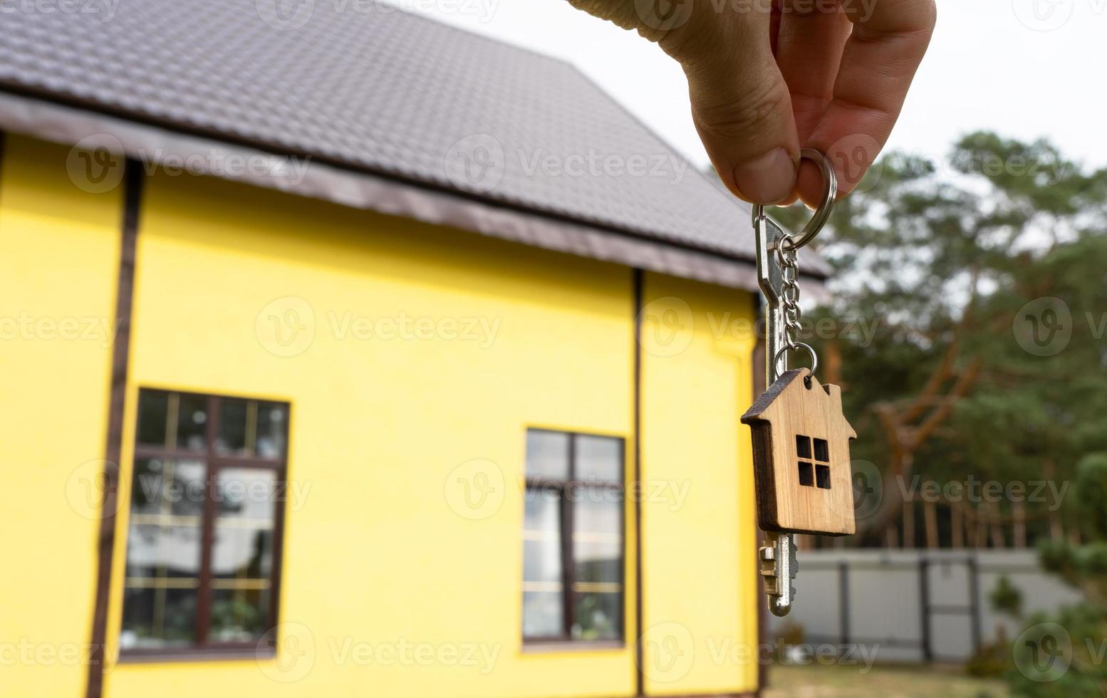 een hand- met de sleutels naar een nieuw huis Aan de achtergrond van een onvoltooid huisje. gebouw, projecteren, in beweging naar een nieuw huis, hypotheek, huur en aankoop echt landgoed. naar Open de deur. kopiëren ruimte foto