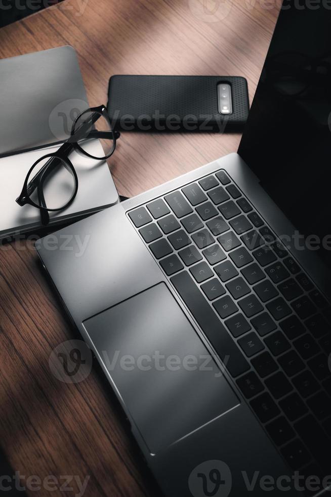 top visie van hout wijnoogst bureau gefocust Aan laptop met kladblok, smartphone en bril. werkplek. werk van huis. kantoor bureau. foto