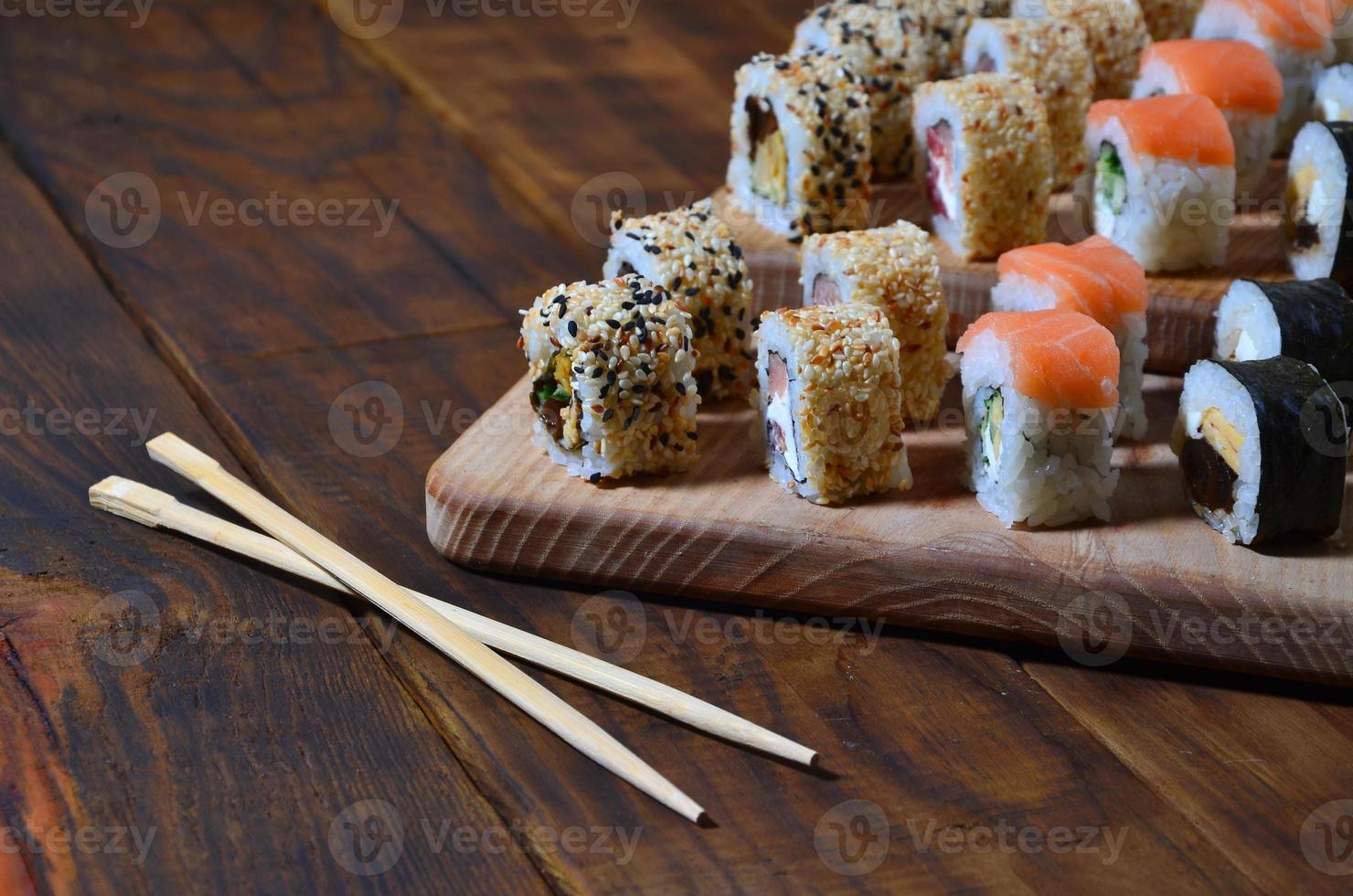 een gedetailleerd schot van een reeks van Japans sushi broodjes en een apparaat voor hun gebruik eetstokjes, welke zijn gelegen Aan een houten snijdend bord Aan een tafel in de keuken van een sushi bar foto