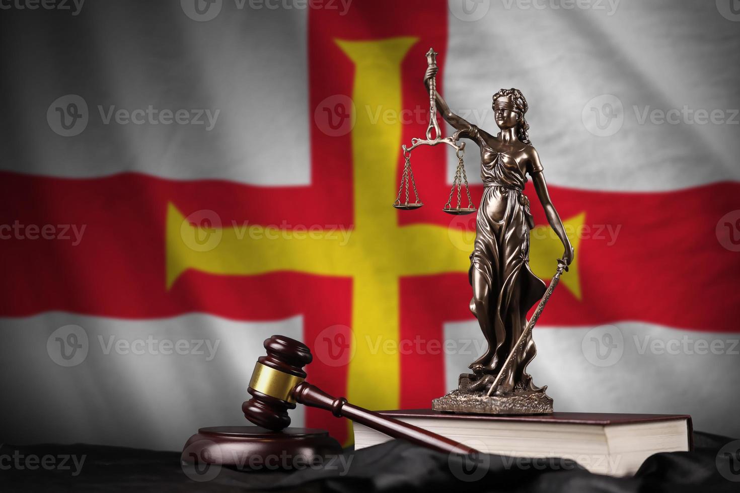 Guernsey vlag met standbeeld van dame gerechtigheid, grondwet en rechter hamer Aan zwart draperie. concept van oordeel en schuld foto