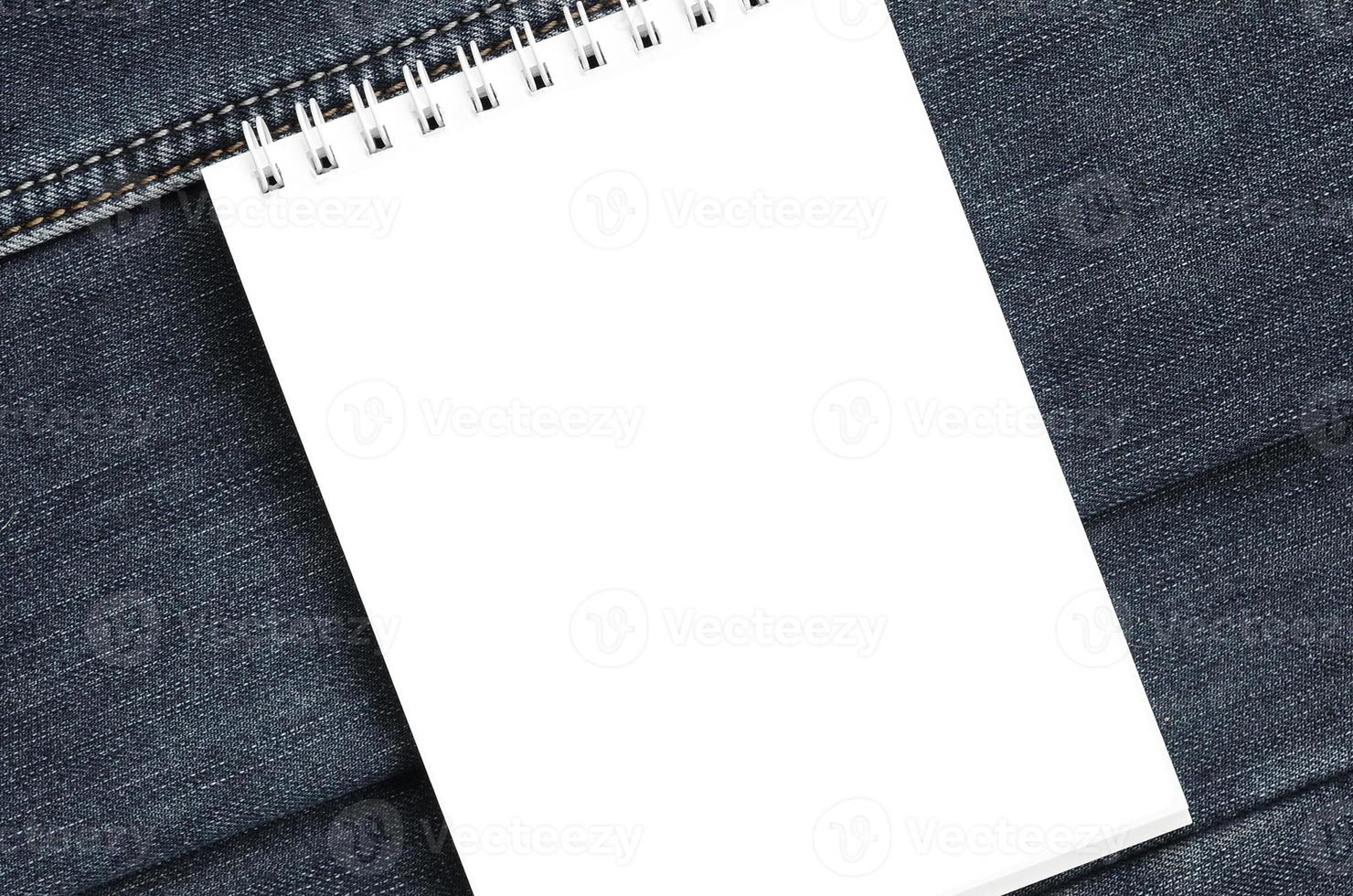wit notitieboekje met schoon Pagina's aan het liegen Aan donker blauw jeans achtergrond. beeld met kopiëren ruimte foto