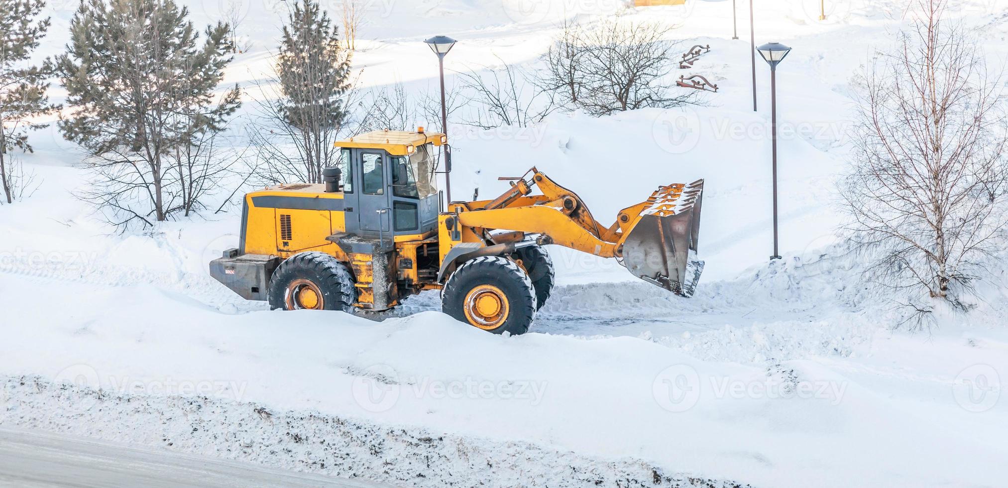 sneeuw opruimen. trekker wist de manier na zwaar sneeuwval. een groot oranje trekker verwijdert sneeuw van de weg en wist de stoep. schoonmaak wegen in de stad van sneeuw in winter. foto