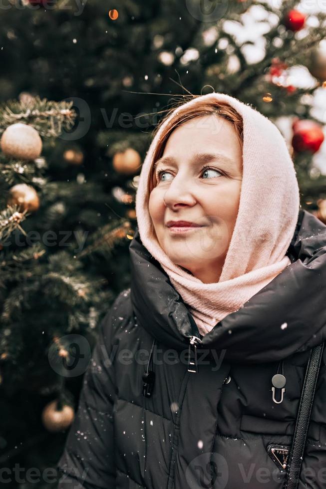 portret van een jong vrouw hartelijk gekleed Aan de straat tegen de achtergrond van Kerstmis decoraties Aan een besneeuwd verkoudheid dag foto