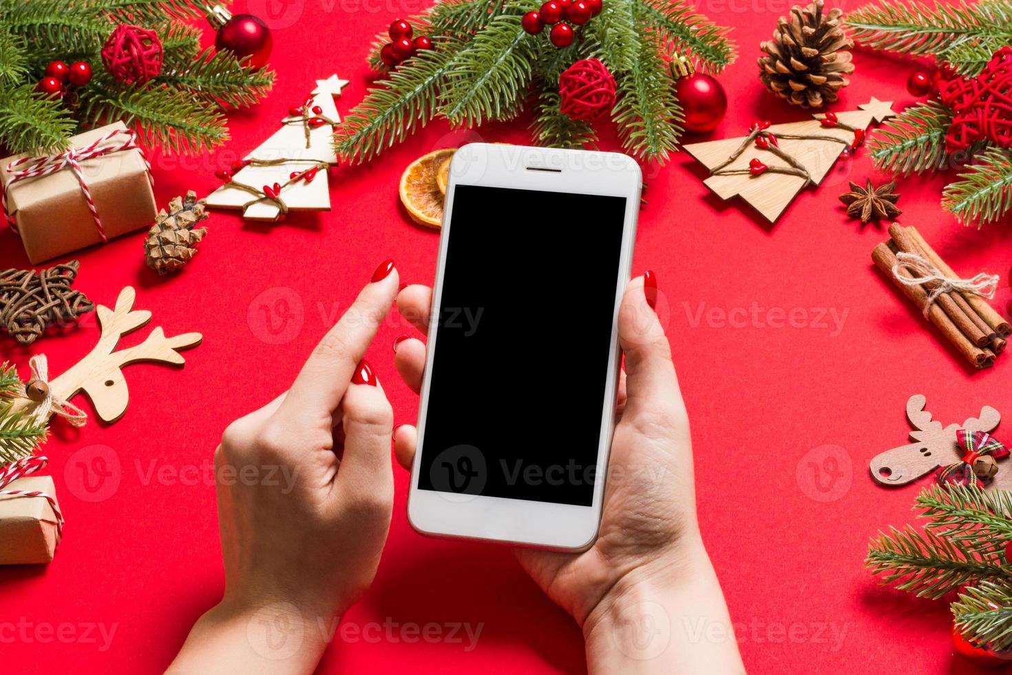 top visie van telefoon in vrouw hand- Aan feestelijk rood achtergrond. Kerstmis decoraties. nieuw jaar tijd vakantie. mockup foto