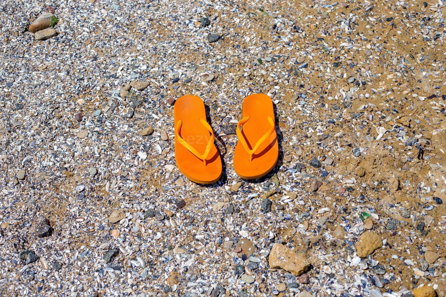 reizen achtergrond met een paar- van oranje slippers in de zand foto