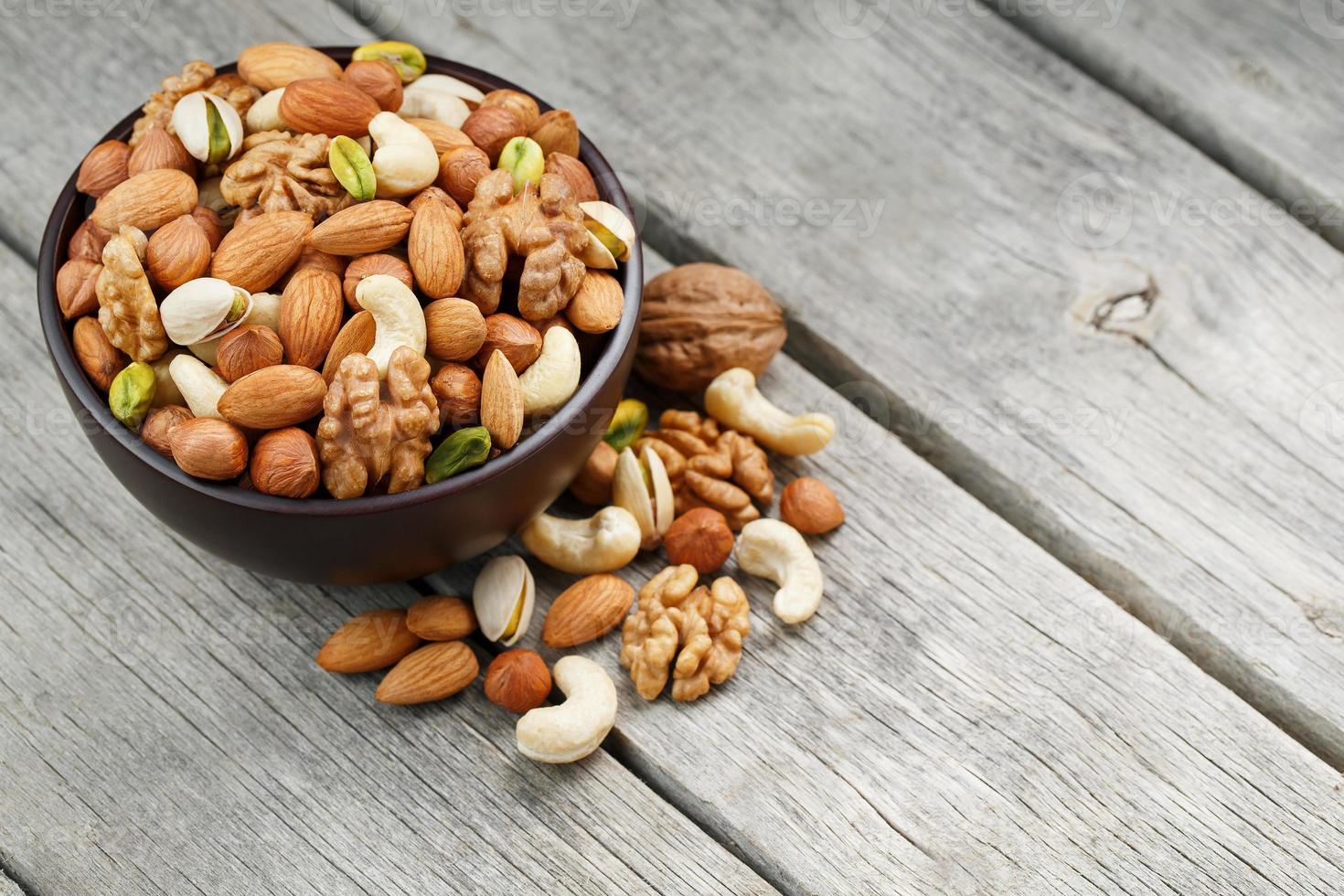 houten kom met gemengd noten Aan een houten grijs achtergrond. okkernoot, pistachenoten, amandelen, hazelnoten en cashewnoten, okkernoot. foto