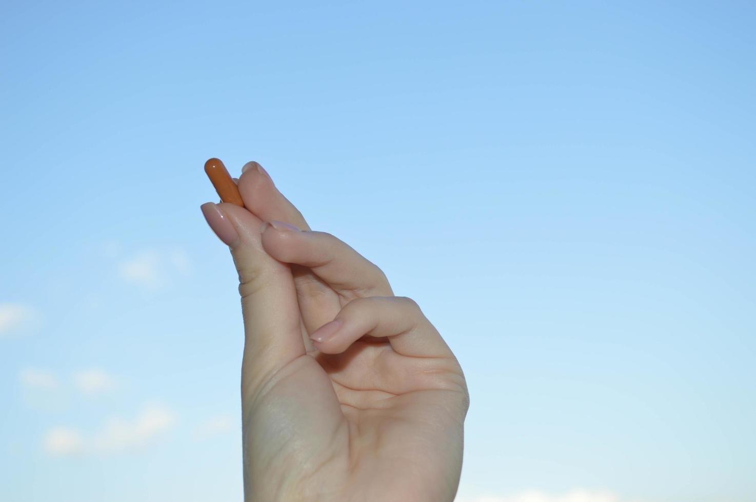 mooi vrouw hand- houdt een medisch farmaceutisch pil capsule van coronavirus covid-19 voor de behandeling van ziekten en virussen Aan een blauw lucht achtergrond foto