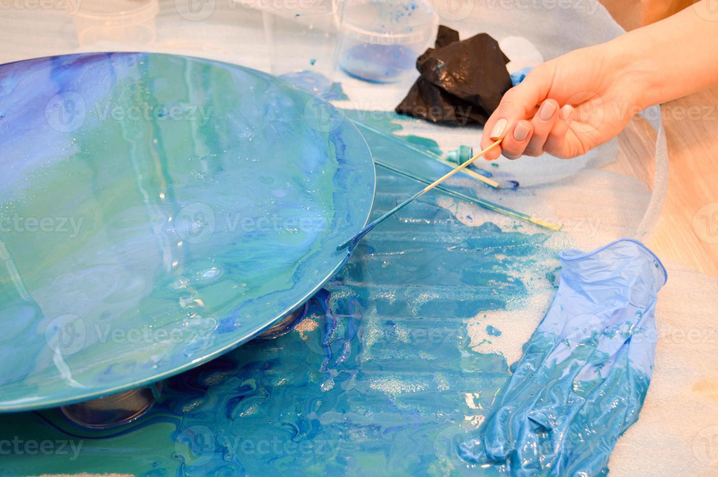 de werkwijze van creëren een eigengemaakt modieus abstract modern patroon geschilderd met een borstel van acryl blauw veelkleurig hars Aan een ronde houten bord foto