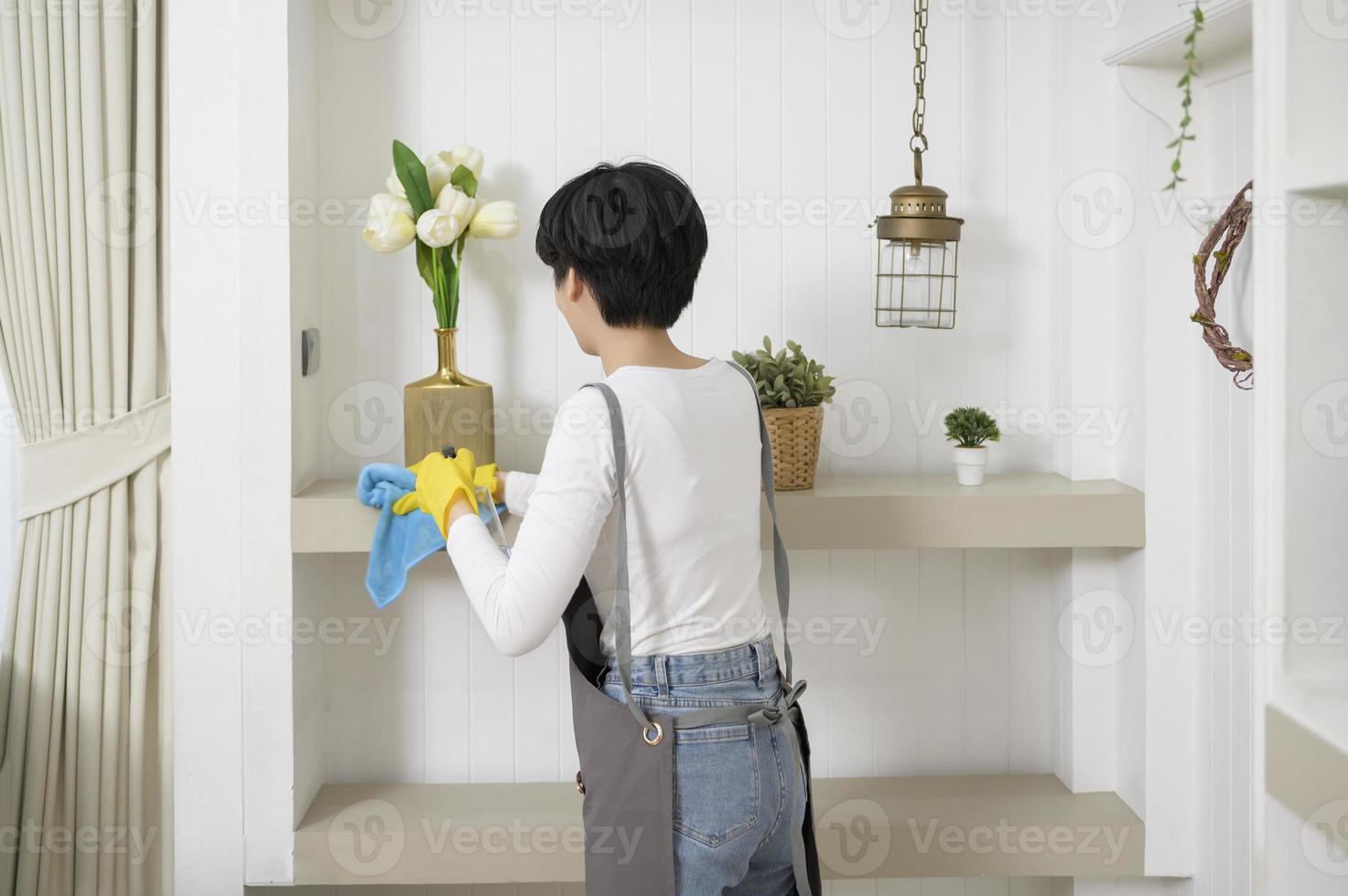 een Aziatisch vrouw met schoonmaak handschoenen gebruik makend van alcohol verstuiven ontsmettingsmiddel naar schoonmaak huis, gezond levensstijl concept foto