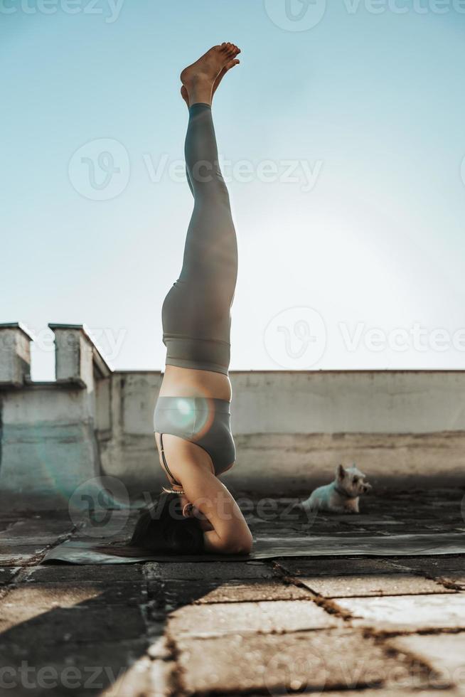 vrouw aan het doen yoga buitenshuis Aan een op het dak terras Bij zonsondergang foto