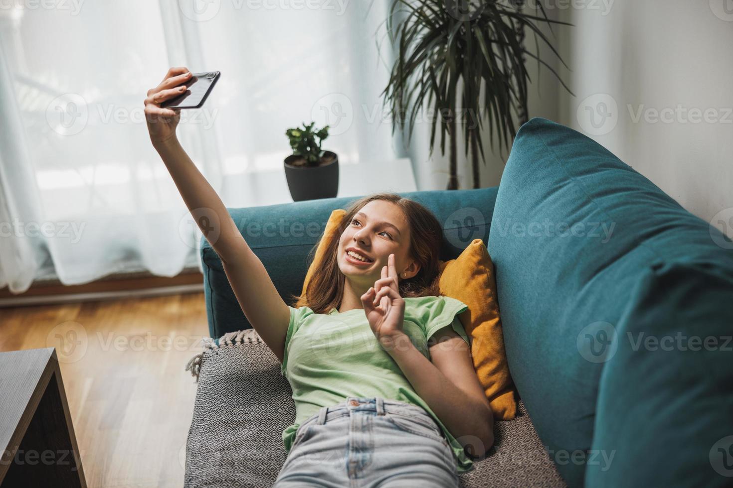 tiener meisje gebruik makend van slim telefoon terwijl hebben vrije tijd tijd Bij haar huis foto