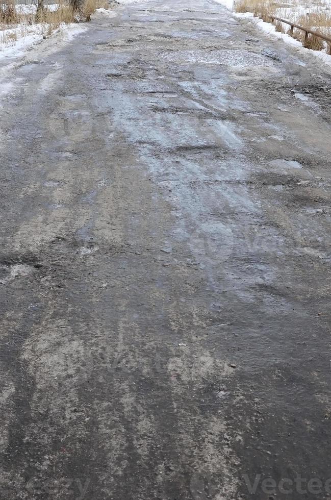 beschadigd asfalt weg met kuilen veroorzaakt door bevriezing en ontdooien cycli gedurende de winter. arm weg foto