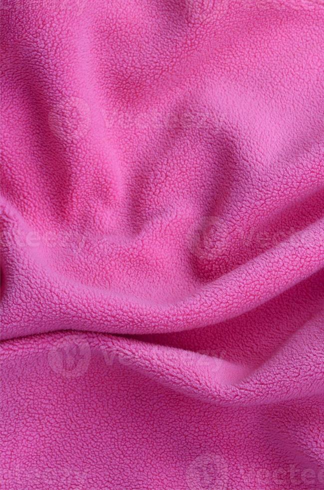 de deken van harig roze fleece kleding stof. een achtergrond van licht roze zacht pluche fleece materiaal met een veel van Verlichting vouwen foto