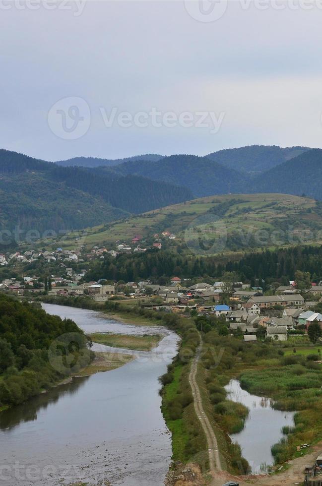 een mooi visie van de dorp van mezhgorye, Karpaten regio. een veel van woon- gebouwen omringd door hoog Woud bergen en lang rivier- foto