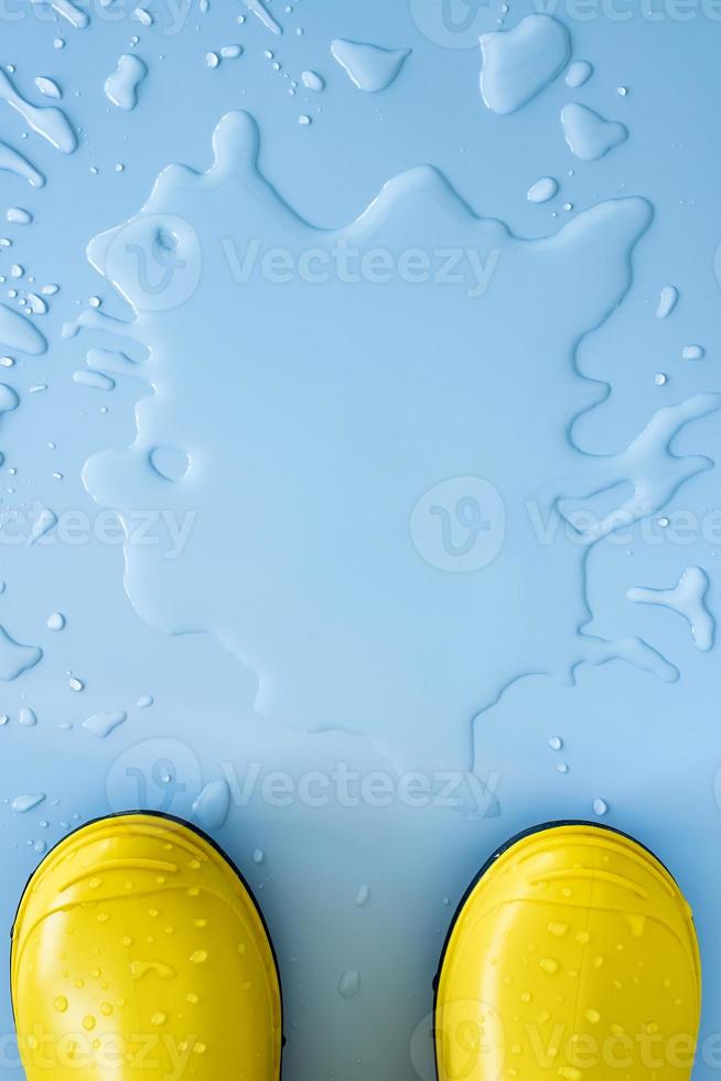 geel rubber waterbestendig laarzen Aan een blauw achtergrond in een plas van water. concept van voorbereiding voor de regenachtig seizoen. kopiëren ruimte. foto