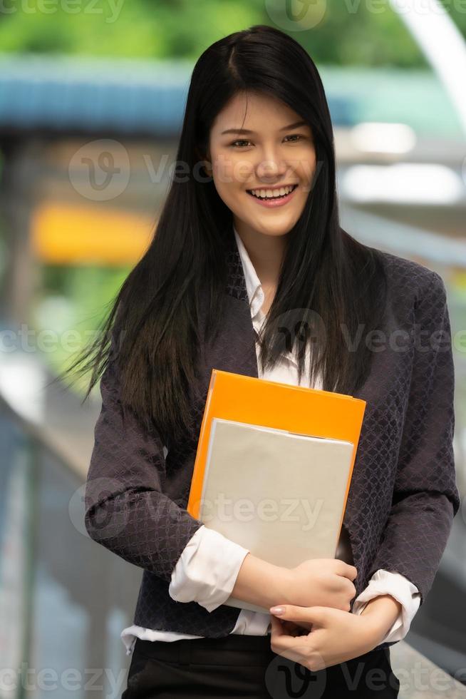 jong Aziatisch vrouw Holding boeken en glimlachen op zoek Bij camera in de Universiteit, mensen onderwijs concept. foto