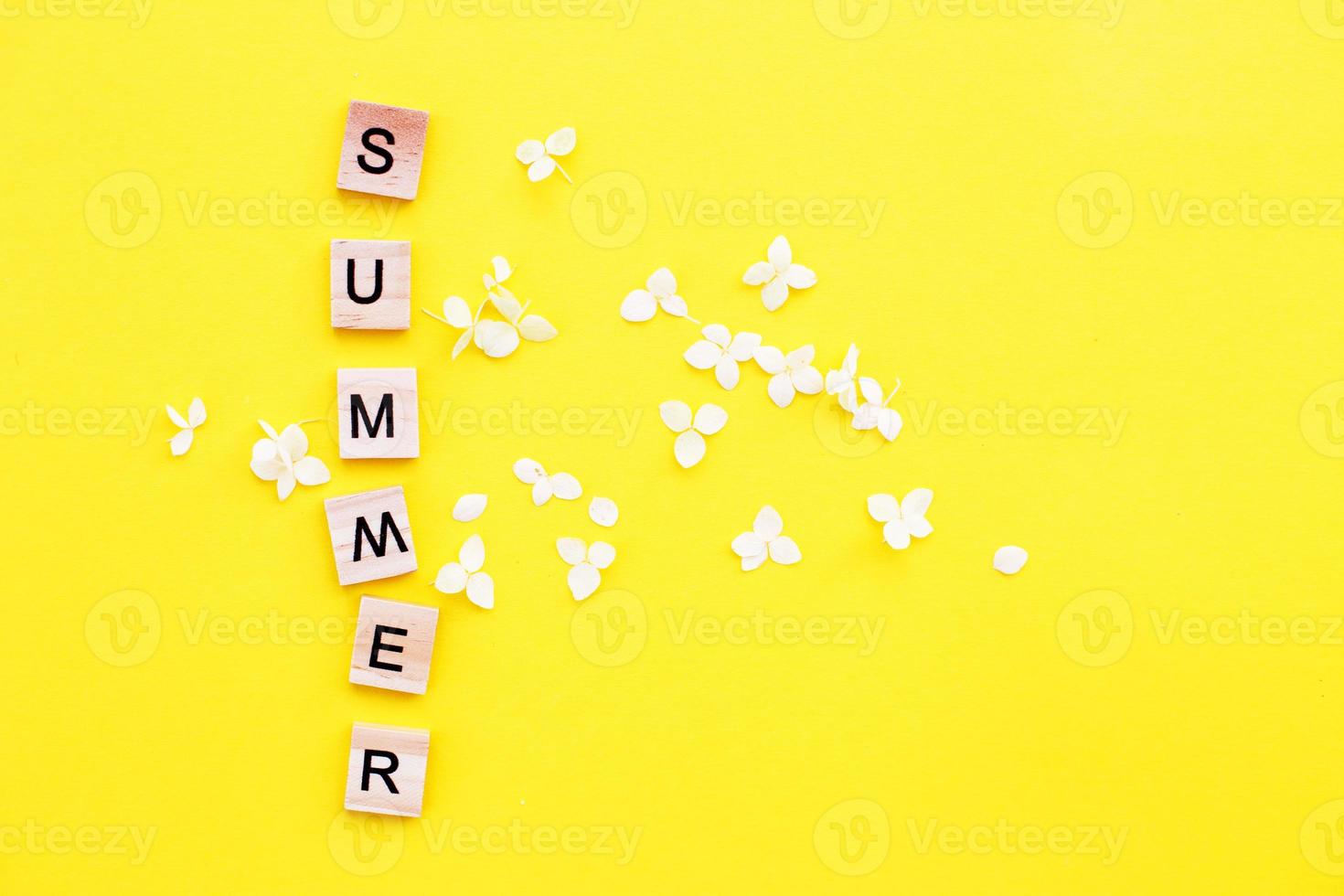 woord zomer geschreven van een houten kubussen met brieven Aan geel achtergrond met een bloemblaadjes van een hortensia bloemen foto