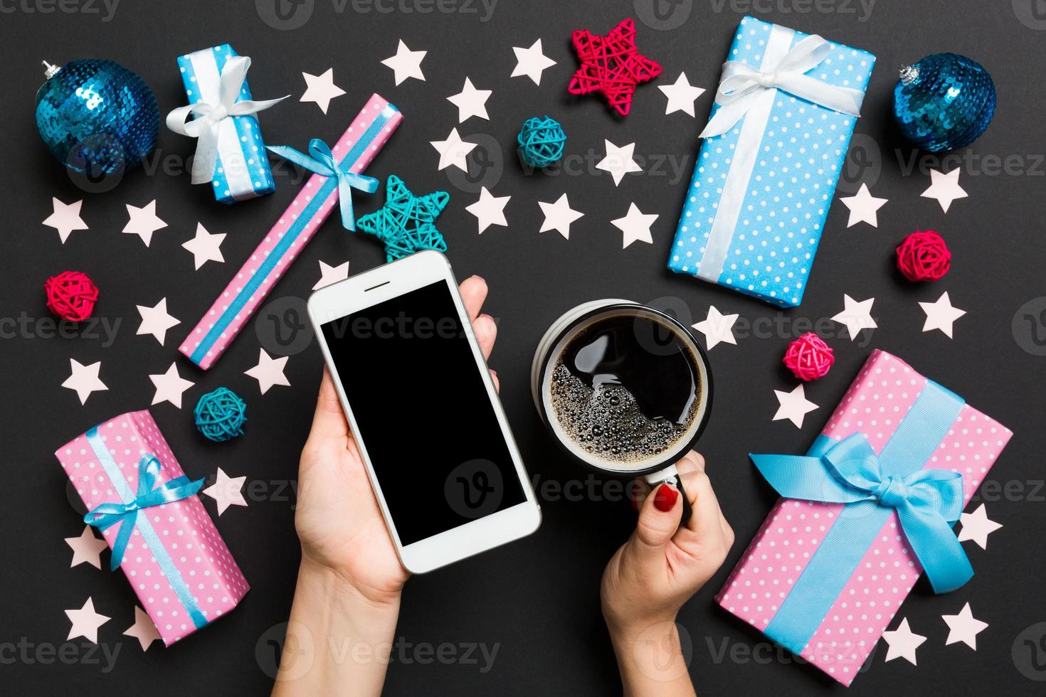 top visie van een vrouw Holding een telefoon in een hand- en een kop van koffie in een ander hand- Aan zwart achtergrond. Kerstmis decoraties en speelgoed. nieuw jaar vakantie concept. mockup foto