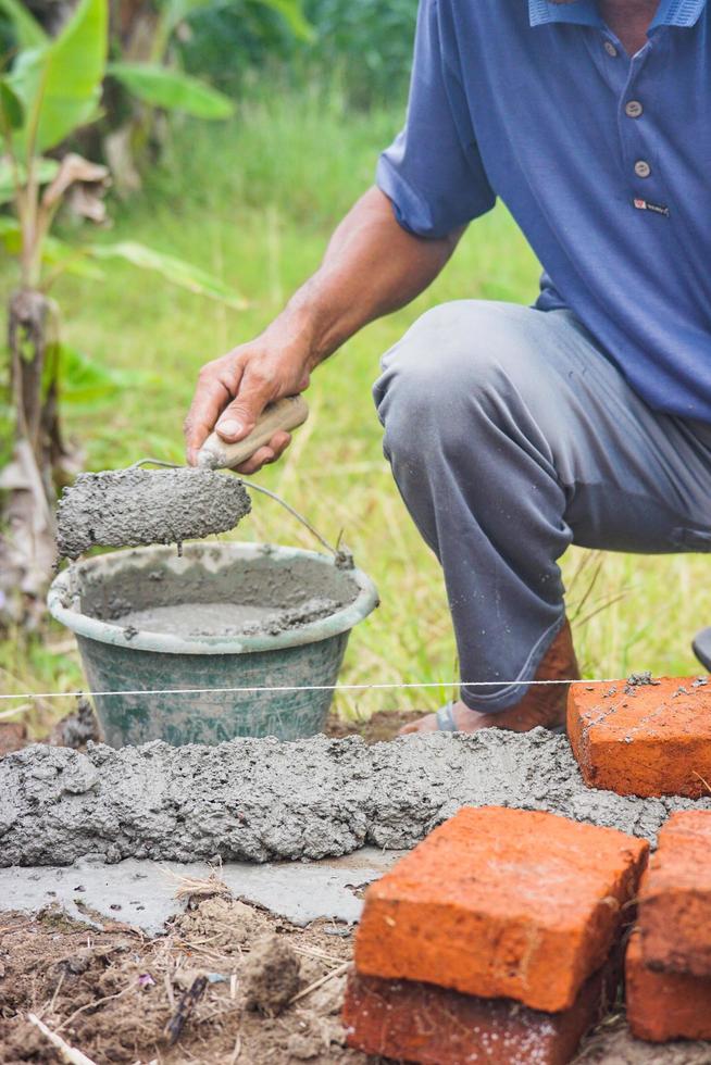 bouw arbeiders installeren bakstenen en cement van rijen van bakstenen Aan buitenkant muren foto