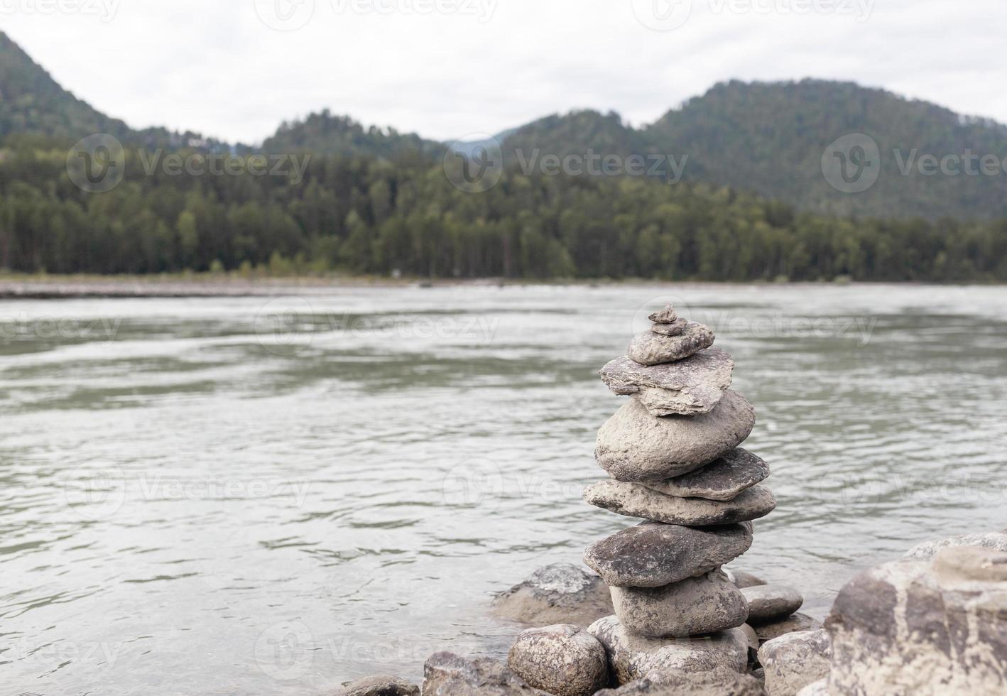 een piramide van kaal stenen gestapeld Aan top van elk ander. stenen gestapeld in de vorm van een piramide Aan de oever van de rivier tegen de achtergrond van bergen net zo balans en balans in natuur, zen, Boeddhisme. foto