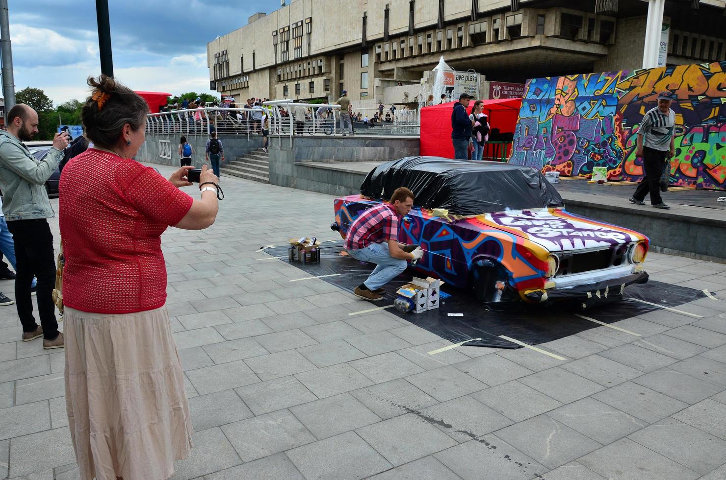 Charkov. Oekraïne - mei 2, 2022 festival van straat kunst. jong jongens trek graffiti Aan de auto lichaam in de stad centrum. de werkwijze van tekening kleur graffiti Aan een auto met aërosol blikjes foto