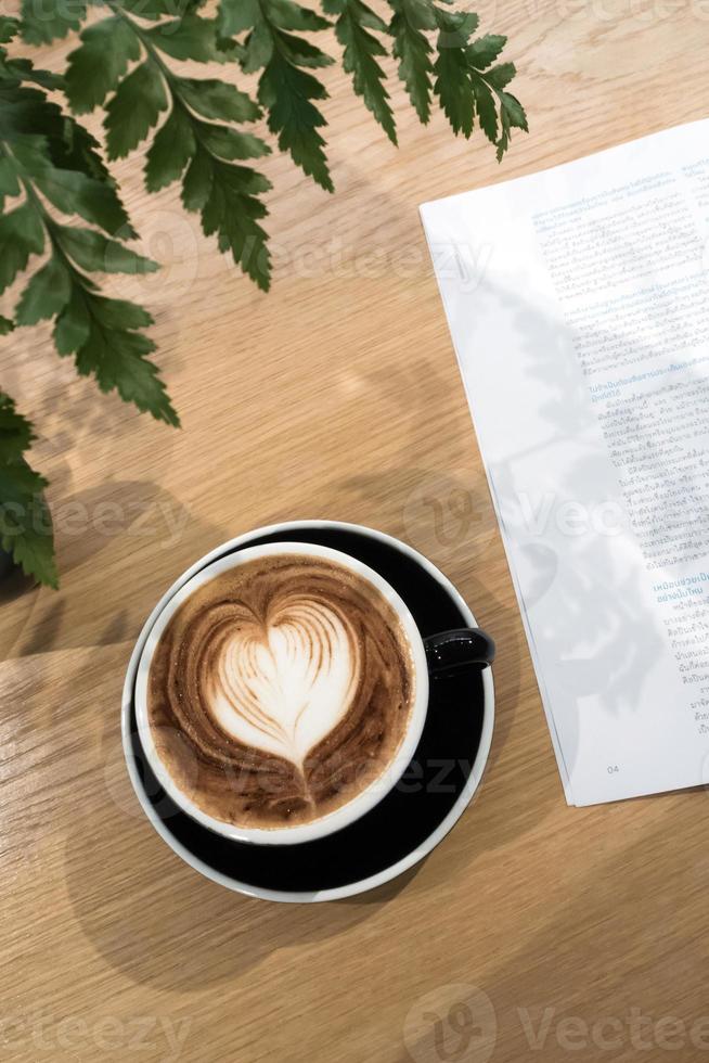 koffie kop en een een deel van boek Aan hout tafel met ornament varen blad foto