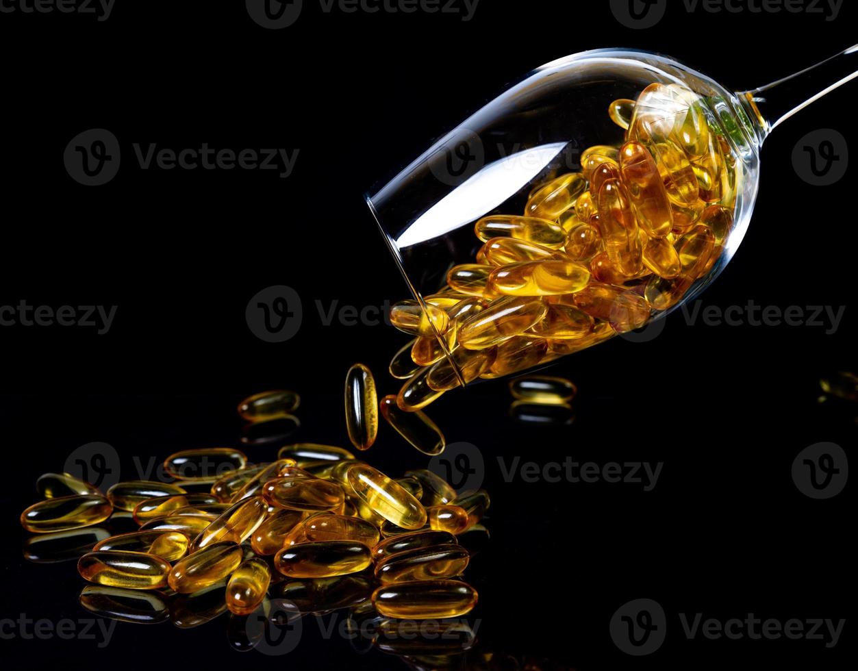 vis olie capsules. geel omega 3 pillen in pot Aan de donker zwart. vis olie capsules in wijnglas glas . in kan. in emmer ampullen foto