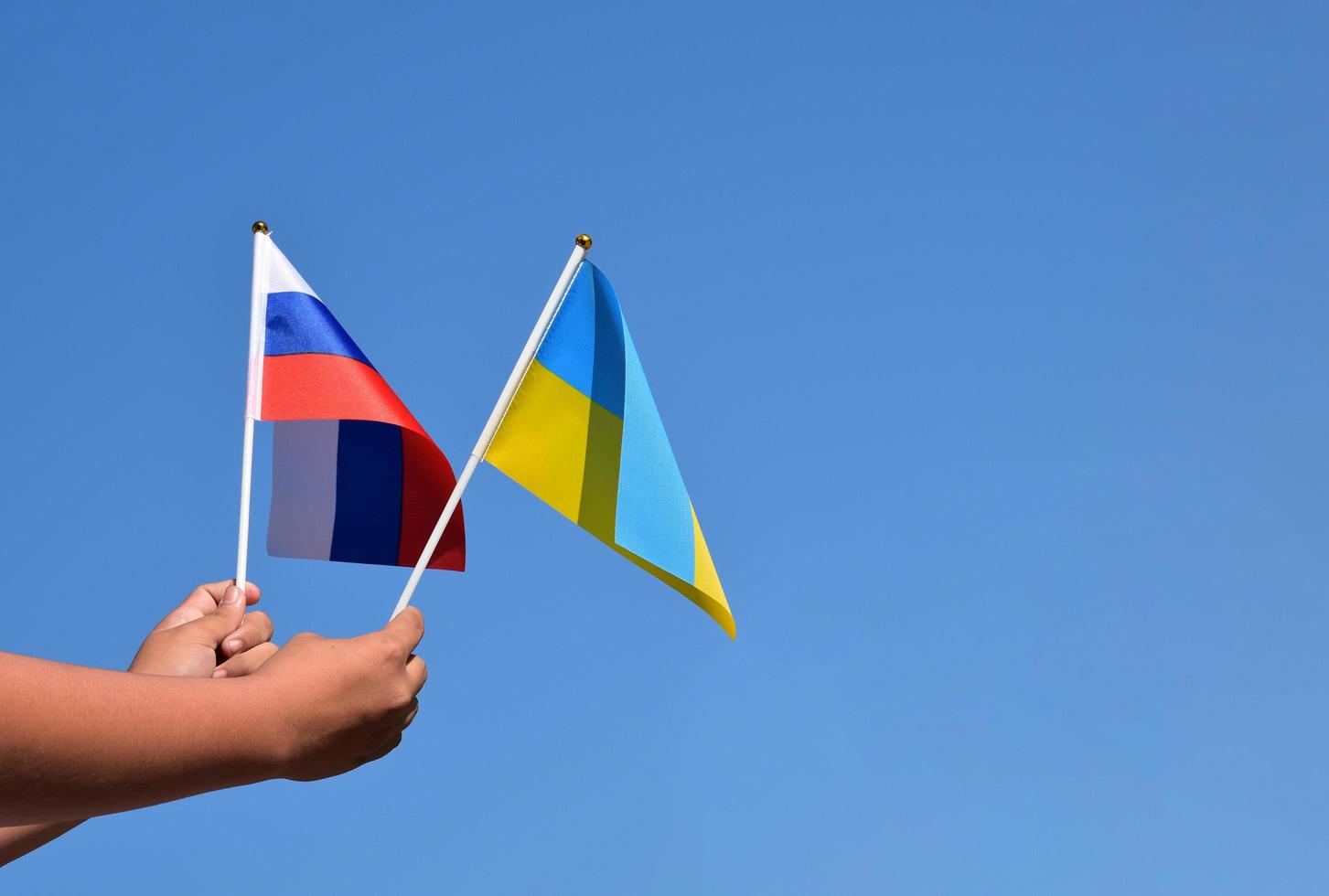 Russisch nationaal vlag en oekraïens nationaal vlag Holding in handen tegen blauwe lucht achtergrond, zacht en selectief focus. foto