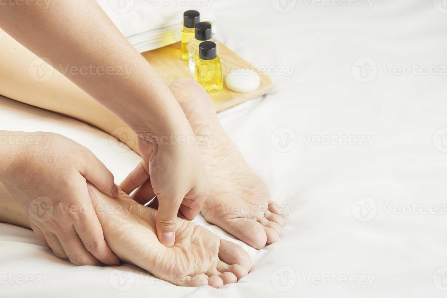 handen van een professioneel voet stimulator met oliën en Gezondheid zorg producten Aan wit bed. concept van Gezondheid zorg, ontspanning, voet spa behandeling. of Product invoering voor vrouwen voet spa foto