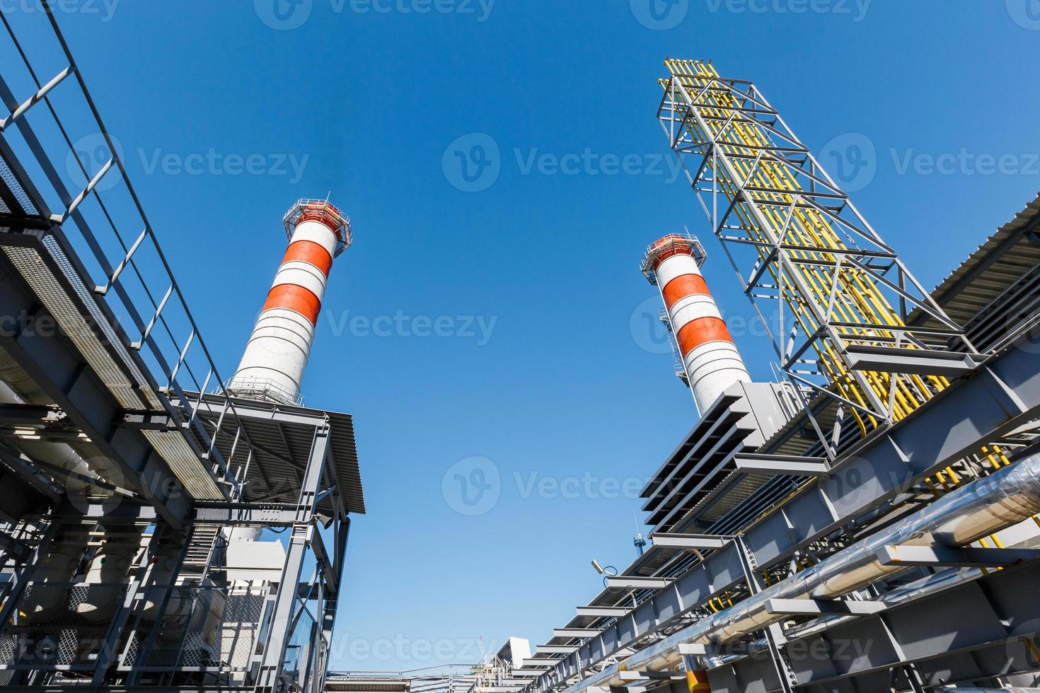 gas- turbine macht fabriek Aan natuurlijk gas- met schoorstenen van rood Wit kleur tegen een blauw lucht Aan een zonnig dag foto