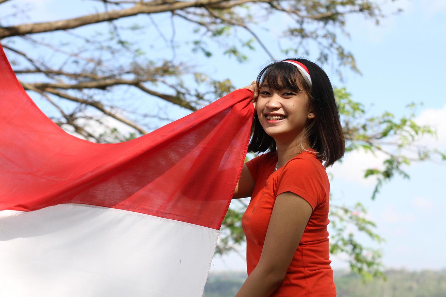 mooi jong Aziatisch vrouw draag- de Indonesisch vlag met een vrolijk gezicht foto