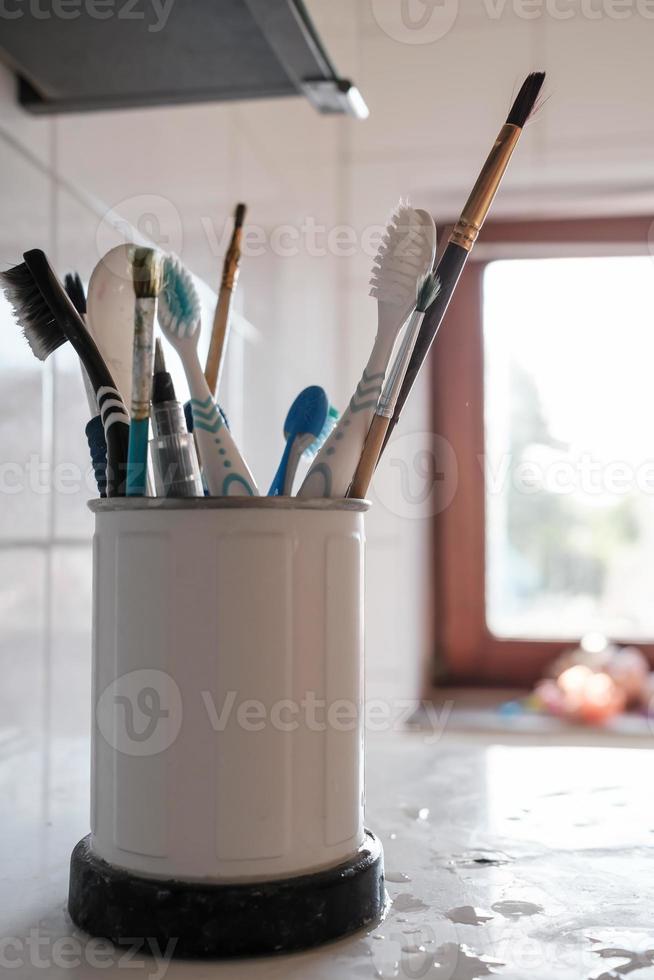 nat artiest borstels en tandenborstels in een metaal houder, Aan de keuken tafel, in natuurlijk licht van de venster. foto