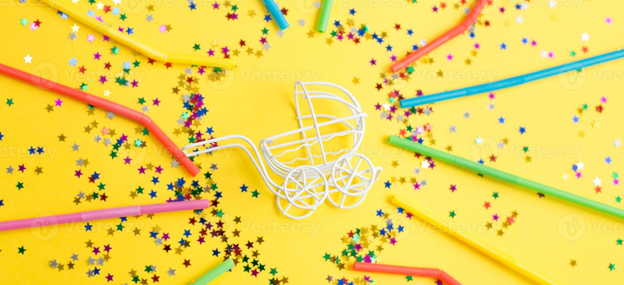 verjaardag feest.baby wandelwagen met sterren confetti pailletten en veelkleurig drinken rietjes Aan geel achtergrond. banier foto